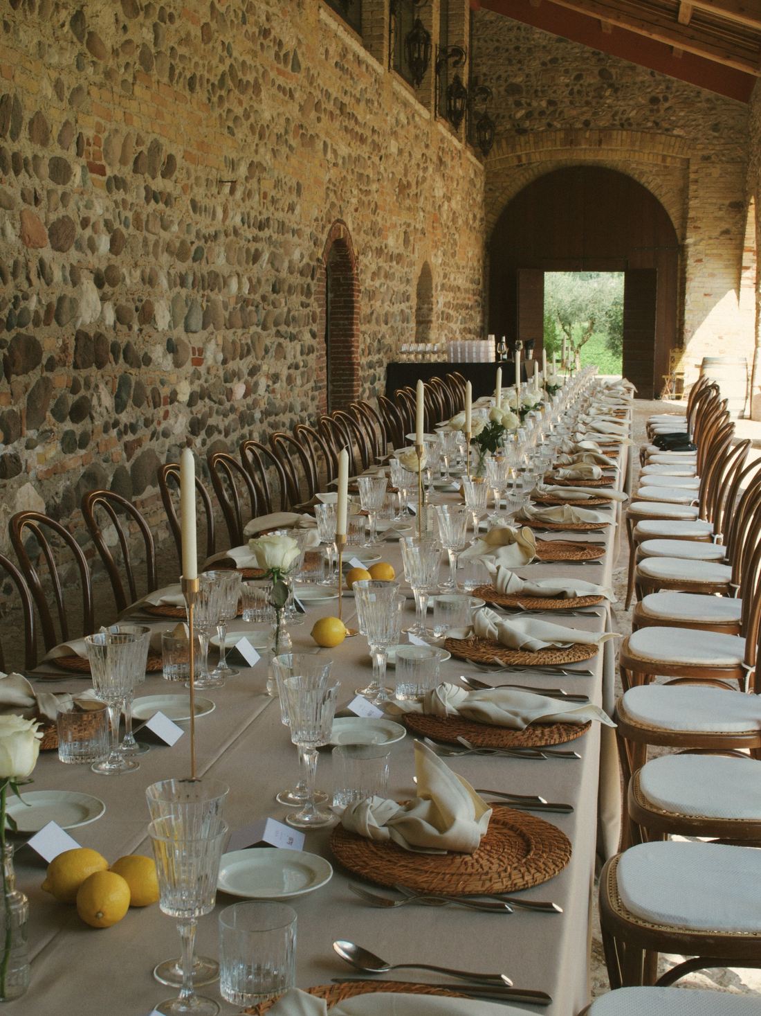 One long table laid down a vaulted stone hall, lemons and rattan on cream linen